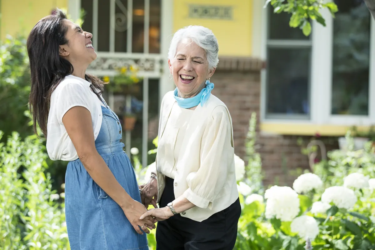 Fotografía de la red Homewatch CareGivers: una cuidadora y una señora mayor se ríen juntas en el jardín de su casa.