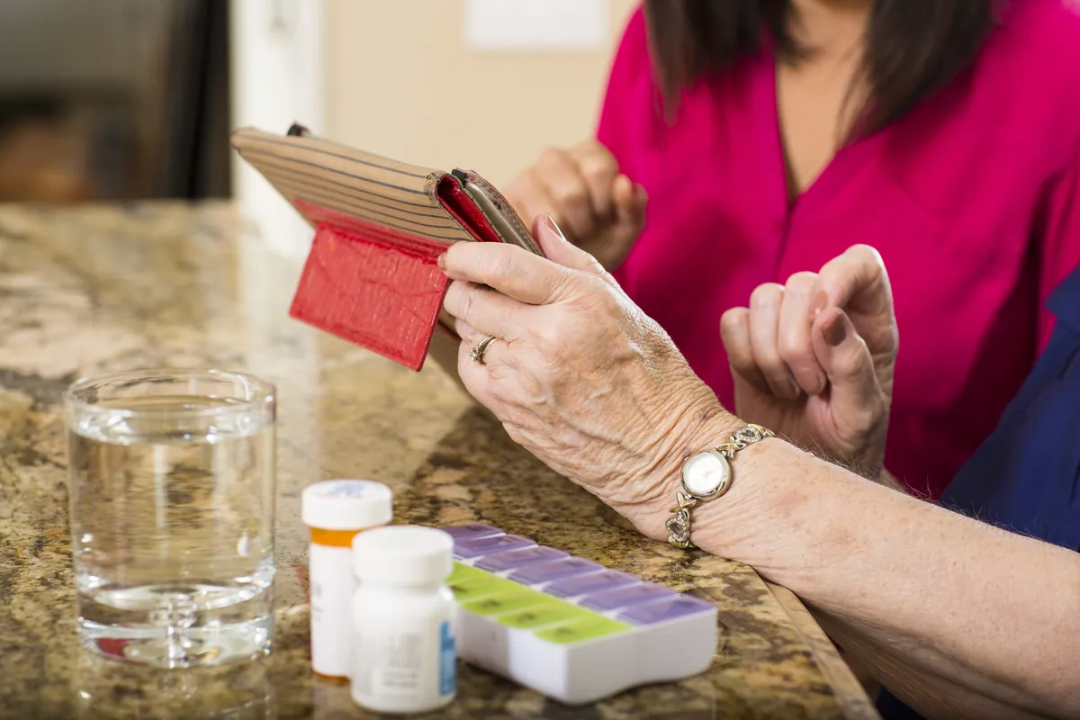 Fotografía de la red Homewatch CareGivers: una cuidadora ayuda a una señora mayor con su organizador semanal de medicamentos.